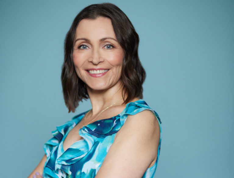 Mia kädet puuskassa hymyillen katsoo kameraan